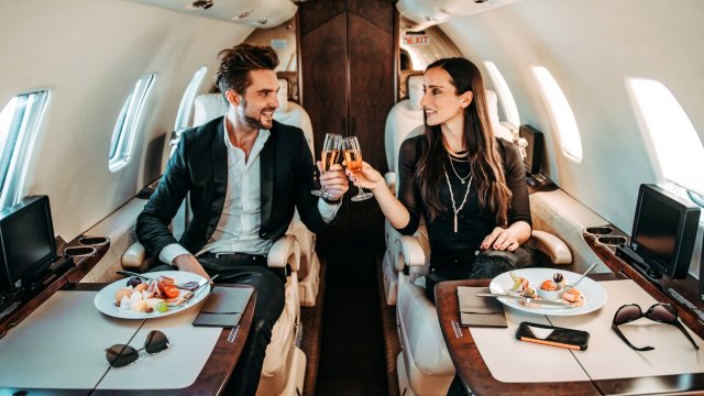 Article thumbnail: Rich couple making a toast with champagne glasses while eating canapes aboard a private jet.