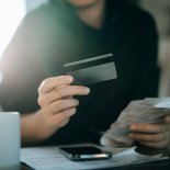 Article thumbnail: Cropped shot of young Asian woman holding credit card and expense receipts, handing personal banking and finance at home. Planning budget, calculating expenses and managing financial bills. Home budgeting. Home finances. Digital banking habits