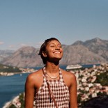 Article thumbnail: Smiling young woman enjoying sunlight against mountain range and sea during vacation