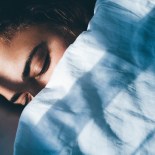 Article thumbnail: Young woman with curly hair sleeps in bed tossing and turning in dream covered with soft blanket in early morning in bedroom at home closeup